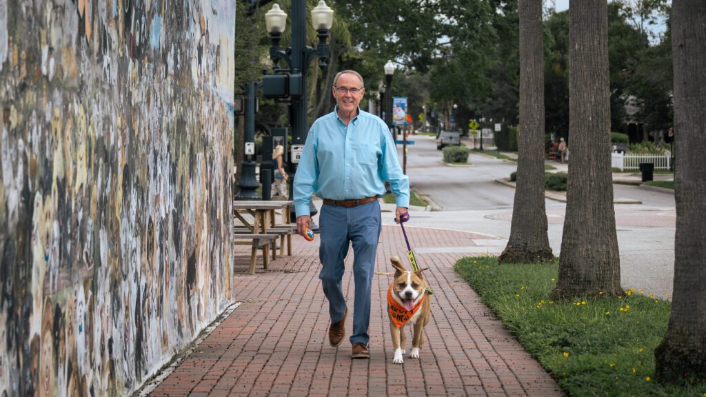 Pinellas County Commission Chair Dave Eggers and K-9 Rollo walk near the Dogedin mural in downtown Dunedin, FL.
