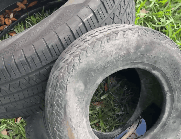 Three tires piled on a lawn with water sitting inside of them