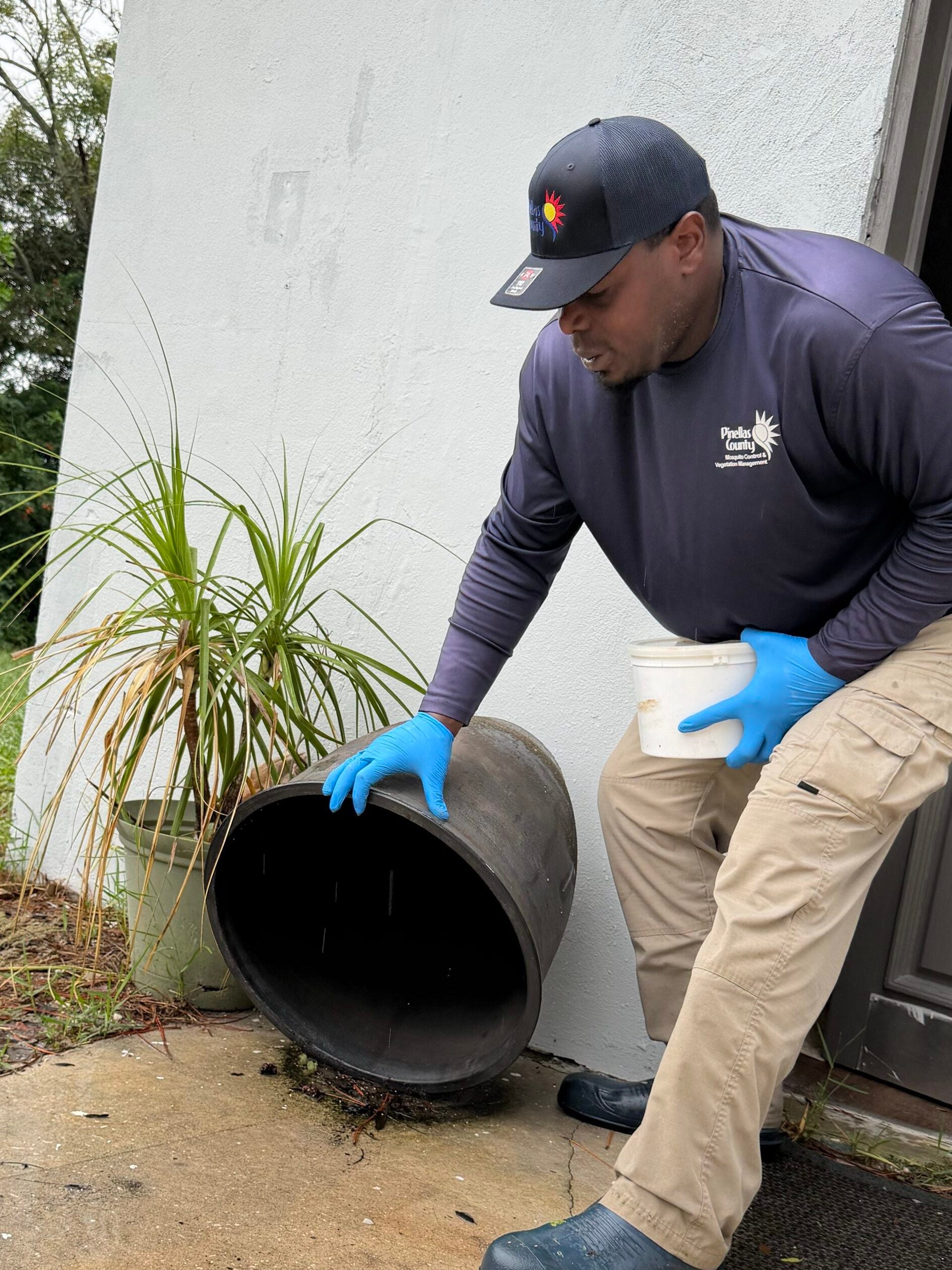 Pinellas County Mosquito Control technician dumps standing water from an empty flower pot during a door-to-door inspection.