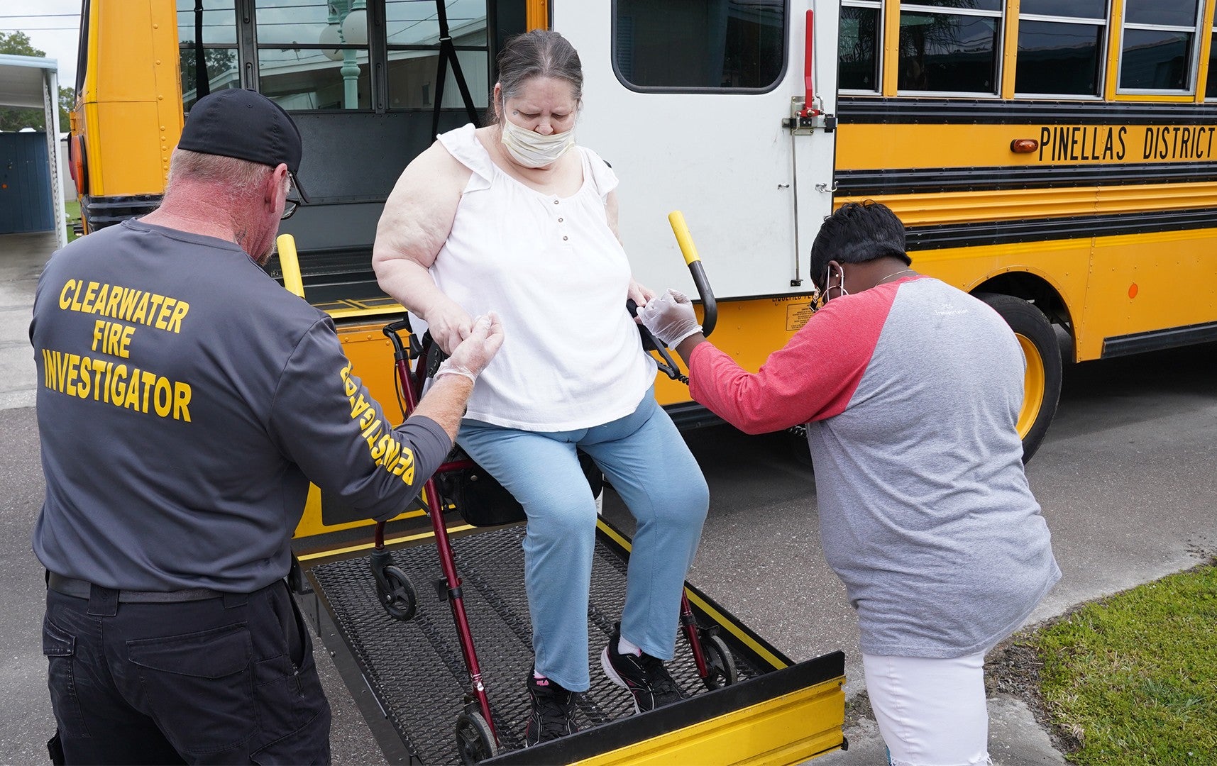 A photo of a woman in a wheelchair being assisted by two people as she gets off of a bus.