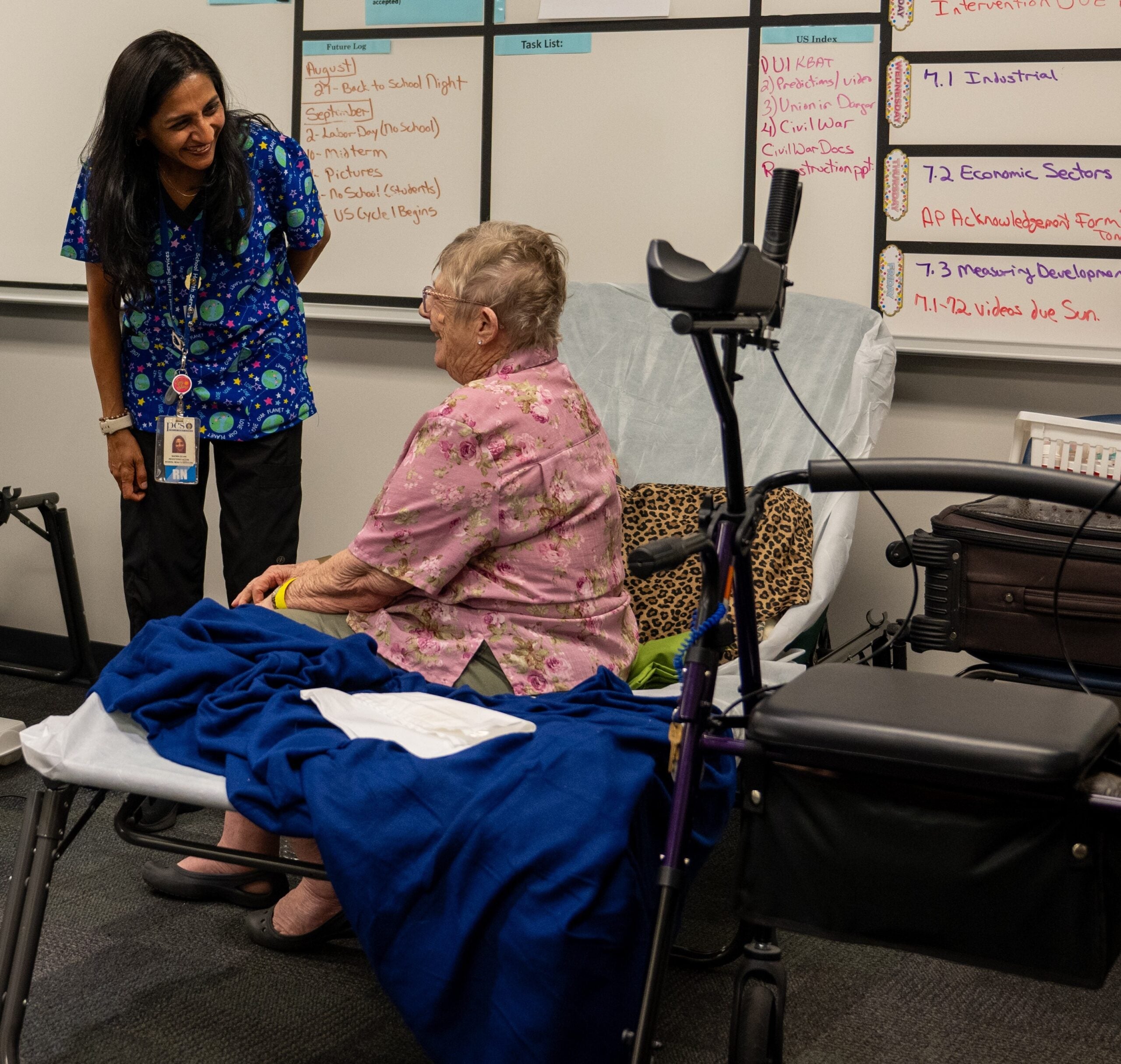 Photo of a woman sitting on the side of a bed laughing with another woman.