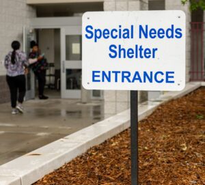 A photo of a sign in front of a building that reads special needs shelter entrance.